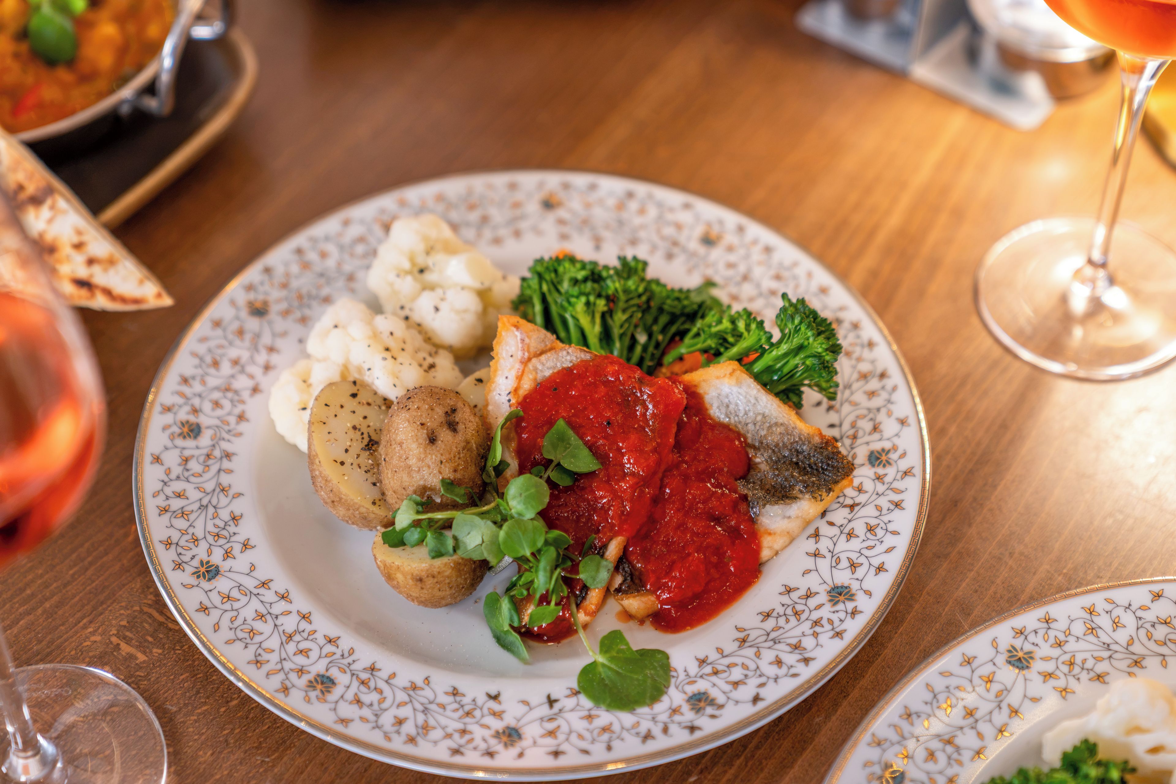 Une assiette contenant du poisson, des pommes de terre, des brocolis et une sauce rouge.