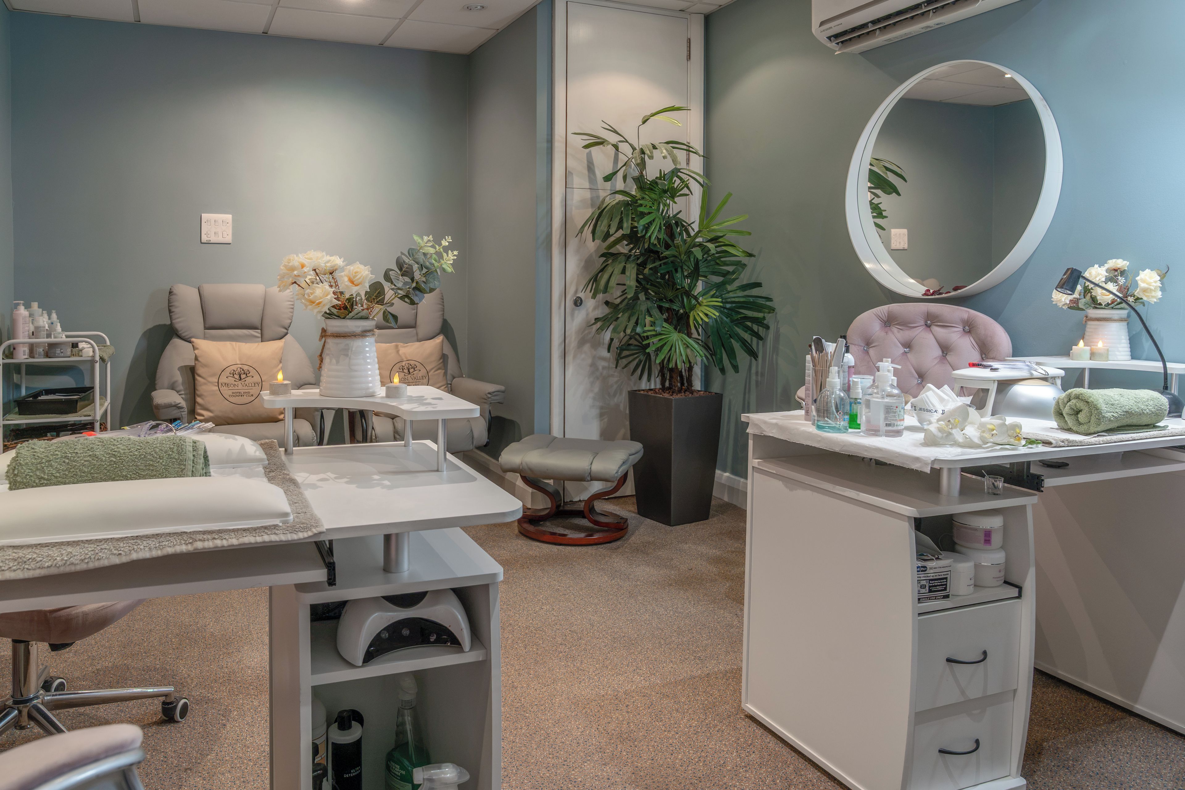 A modern spa room with a massage table, a chair, a vanity with a mirror, and a plant.