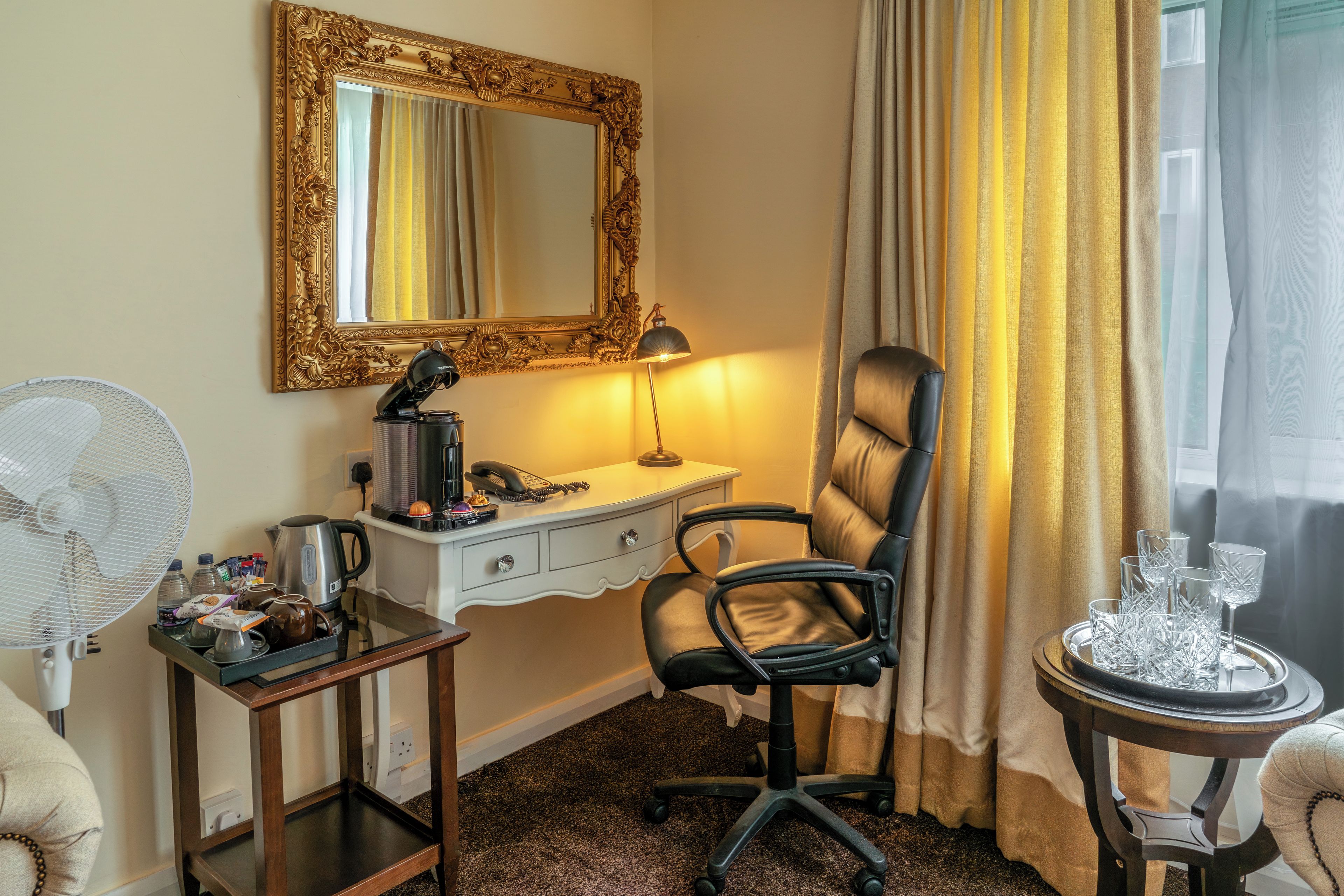 Une chambre d’hôtel équipée d’un bureau, d’une chaise, d’un ventilateur et d’une table avec des verres.