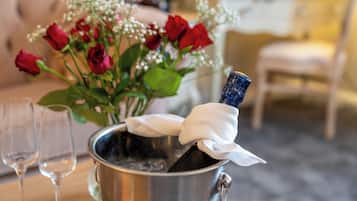 A champagne bottle in a metal bucket with a white cloth, red roses, and two empty glasses on a table.