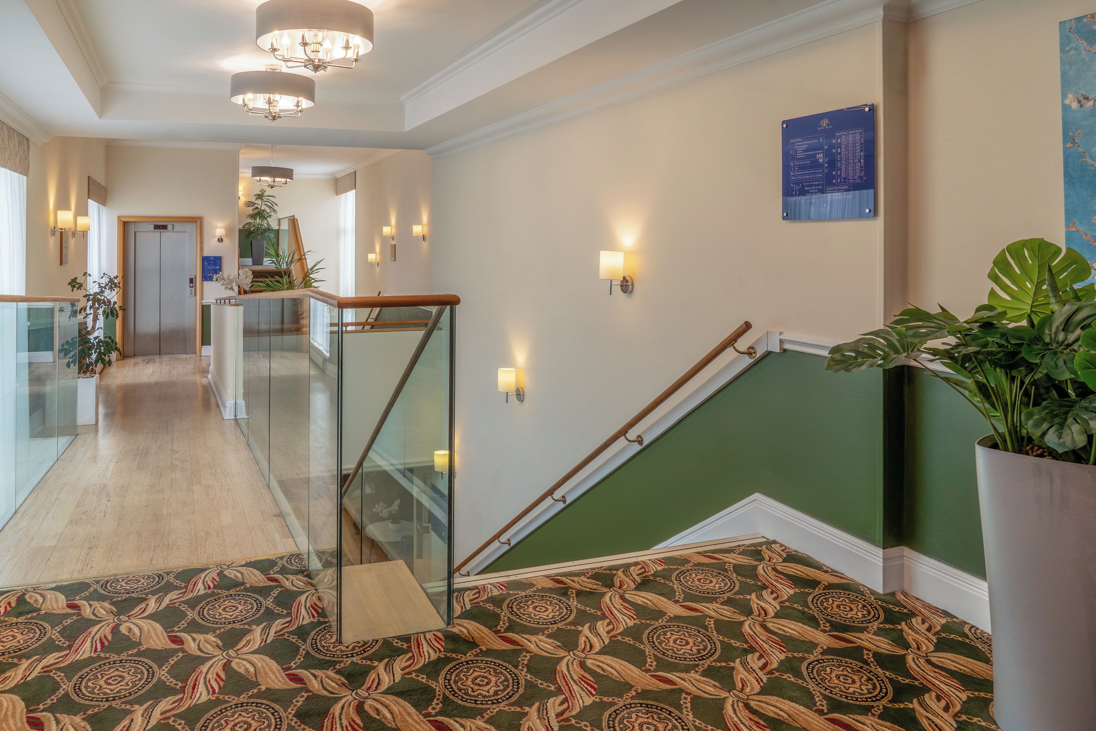 Un hall d’hôtel avec un escalier, un comptoir d’accueil et un panneau d’information fixé au mur.