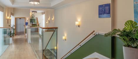 Un hall d’hôtel avec un escalier, un comptoir d’accueil et un panneau d’information fixé au mur.