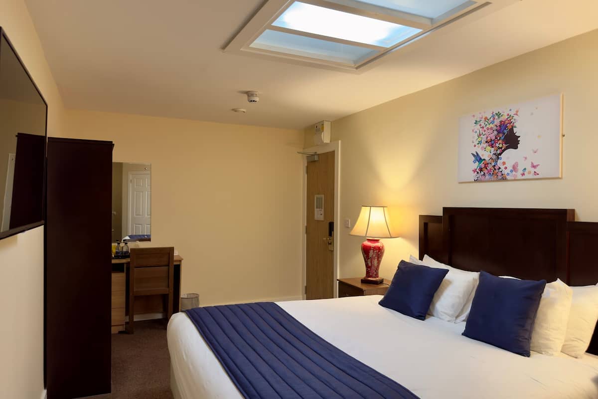A hotel room with a bed, a desk, a lamp, and a painting on the wall.