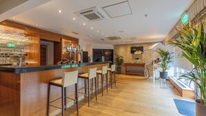 A bar area with a long counter, multiple stools, and a variety of bottles and glasses. - Meon Valley Hotel, Spa & Golf (Southampton)