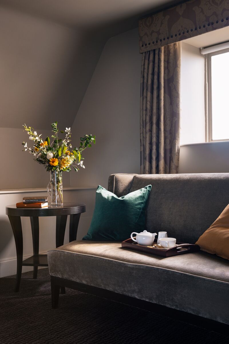 Une pièce confortable avec un canapé, une petite table sur laquelle est posé un vase de fleurs et une fenêtre avec des rideaux.