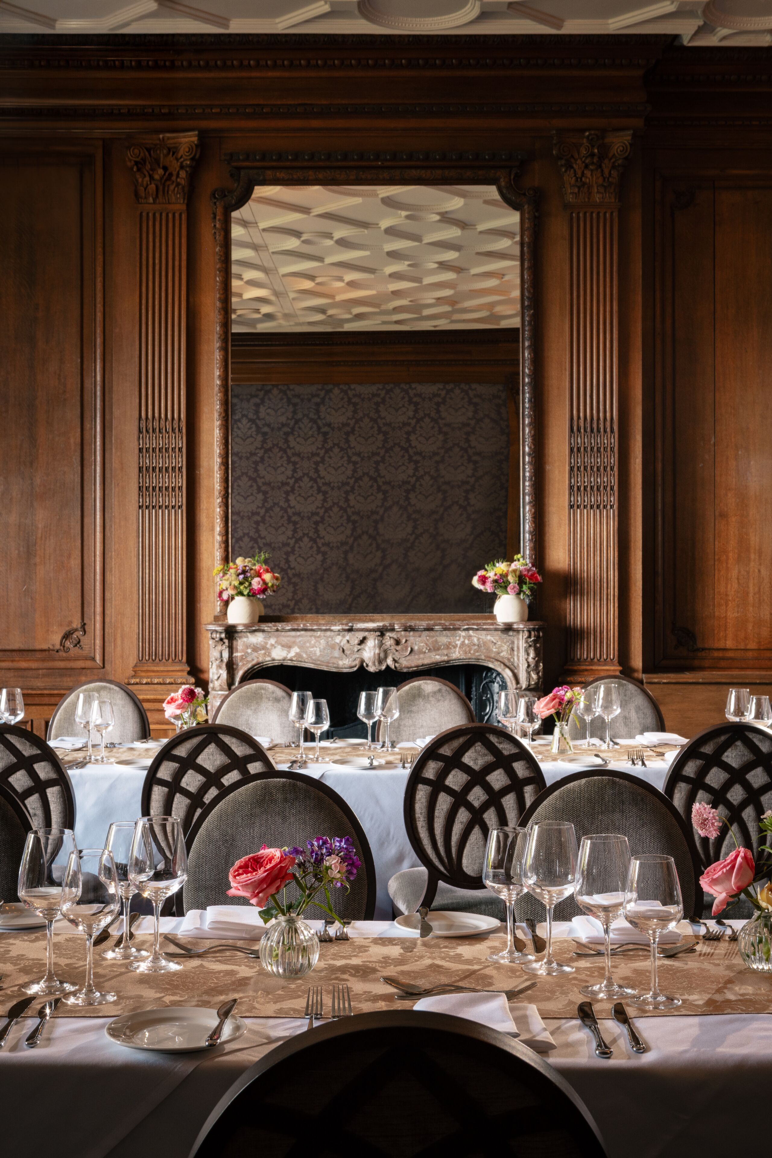 Uma sala de jantar formal com lareira, painéis de madeira e um candelabro.