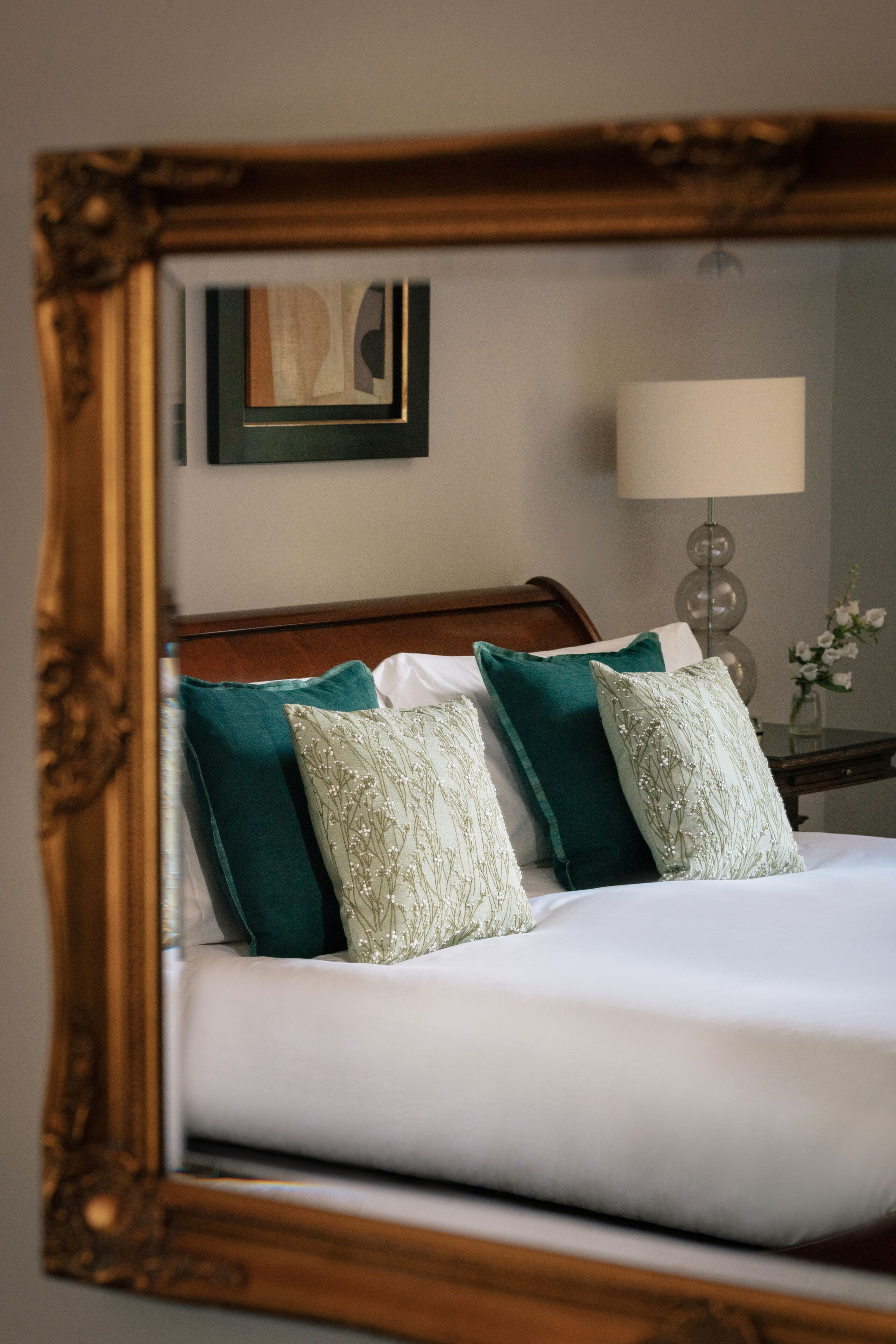A neatly made bed with green and white pillows, a wooden headboard, and a framed picture on the wall.