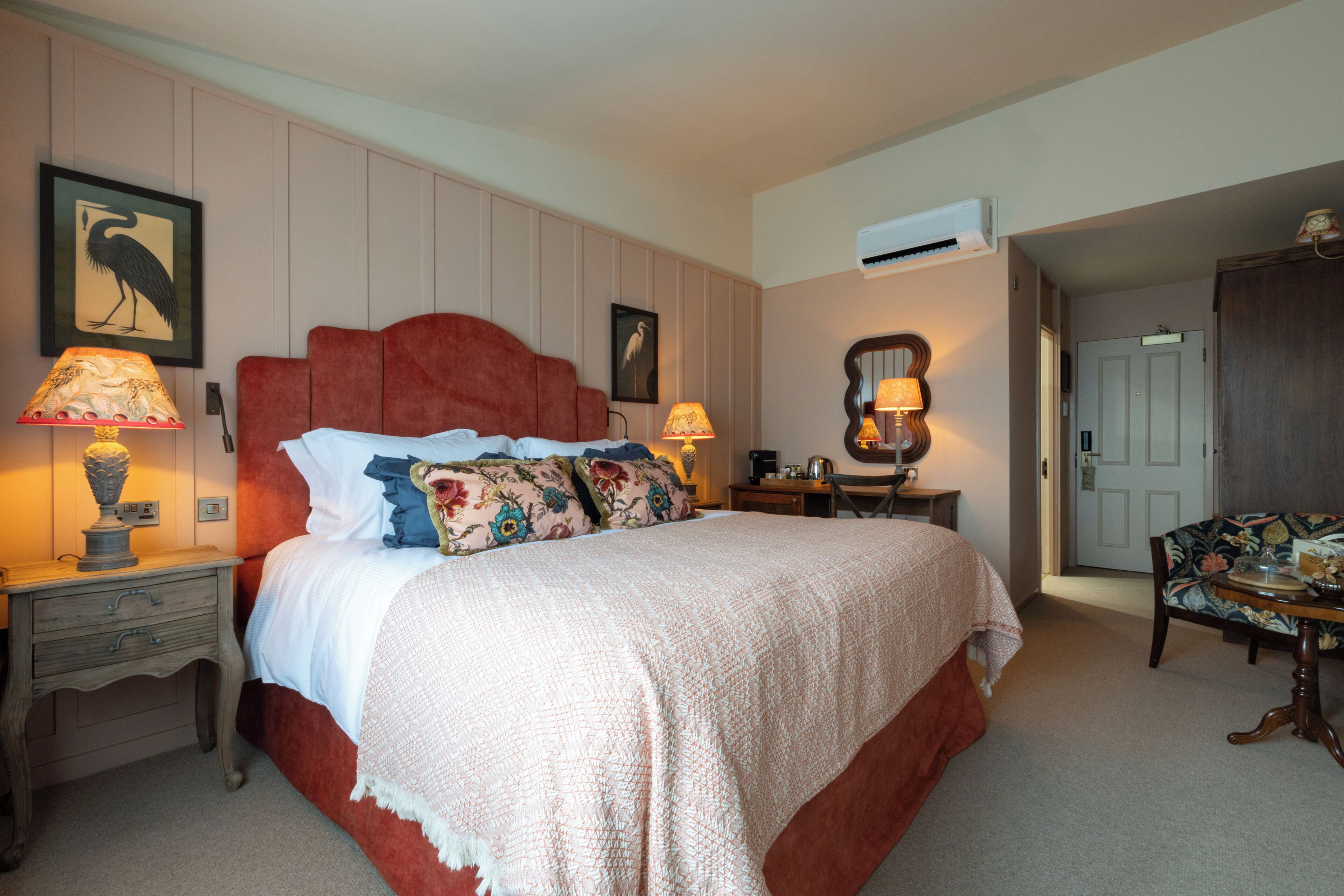 A bedroom with a large bed, two bedside tables with lamps, a chair, a desk, and a door.