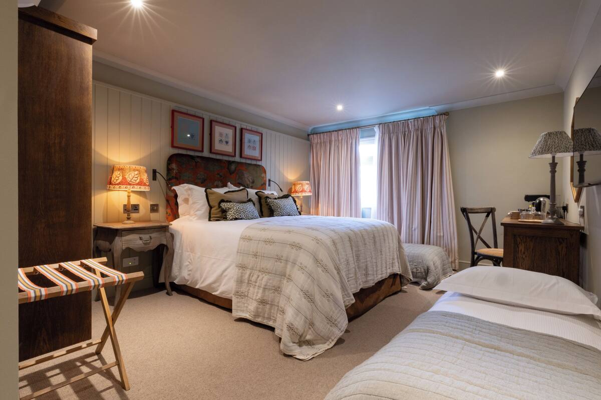 Een slaapkamer met een groot bed, een kleiner bed, een houten garderobe, een nachtkastje, een lamp en een spiegel.
