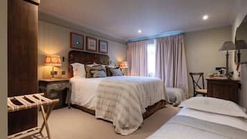 Een slaapkamer met een groot bed, een kleiner bed, een houten garderobe, een nachtkastje, een lamp en een spiegel.