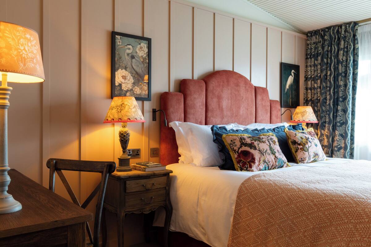 Een netjes ingerichte hotelkamer met een bed, kussens, een nachtkastje, een lamp en een stoel.