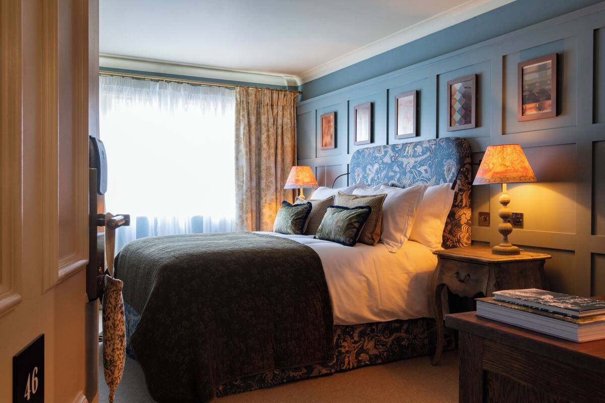 Een hotelkamer met een bed, twee bedlampjes, een nachtkastje en een deur met een nummer.