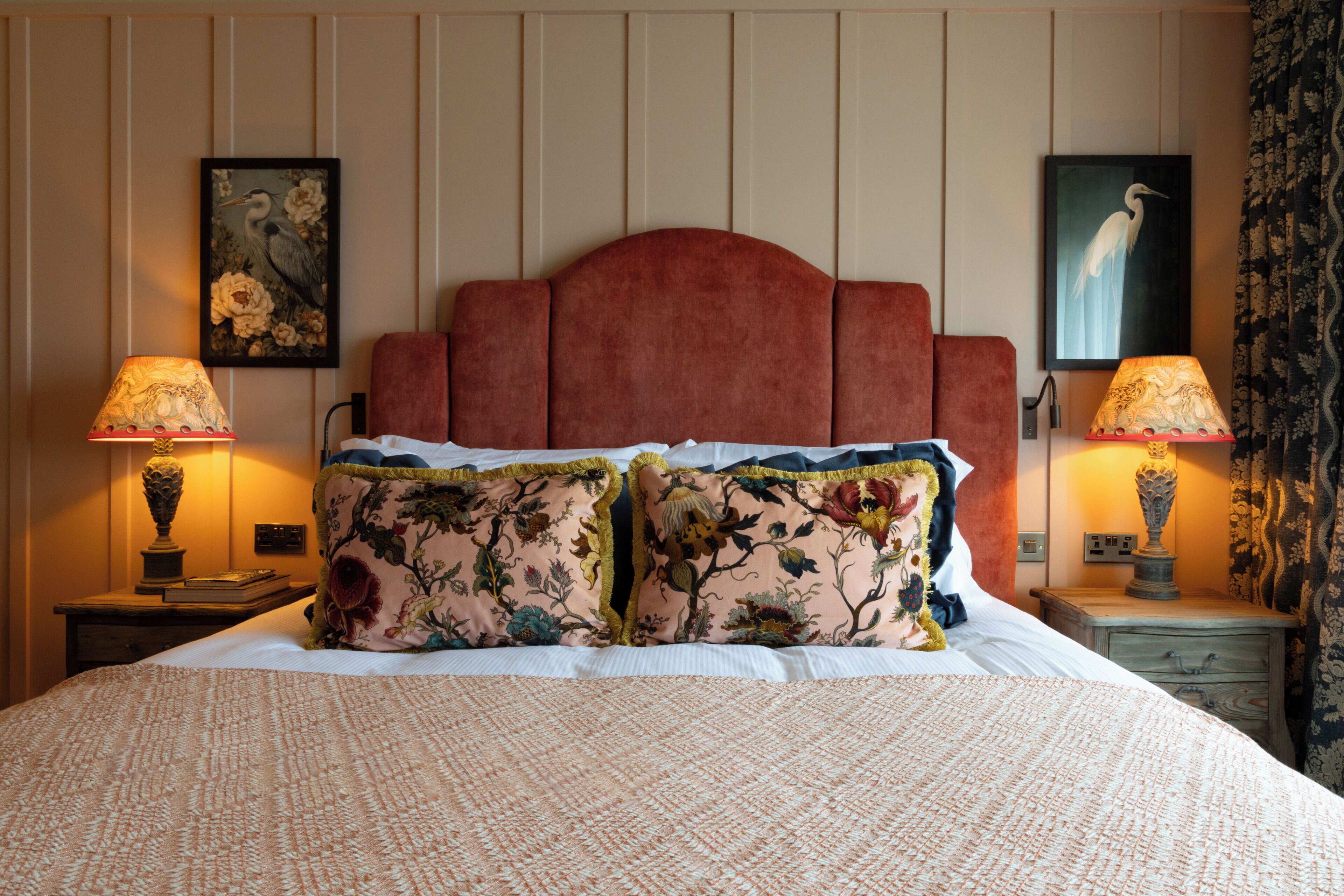 A bed with a red headboard, two nightstands with lamps, and floral artwork on the walls.