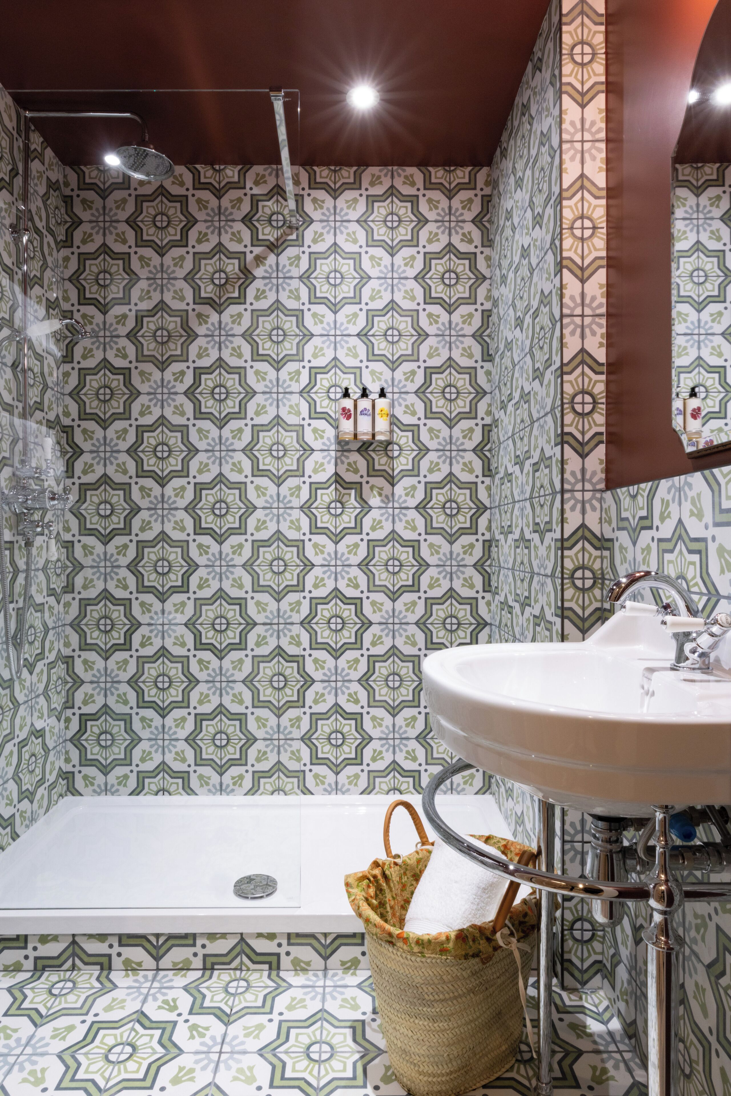 Une salle de bain avec des carreaux décorés, une douche, un lavabo et un panier suspendu.