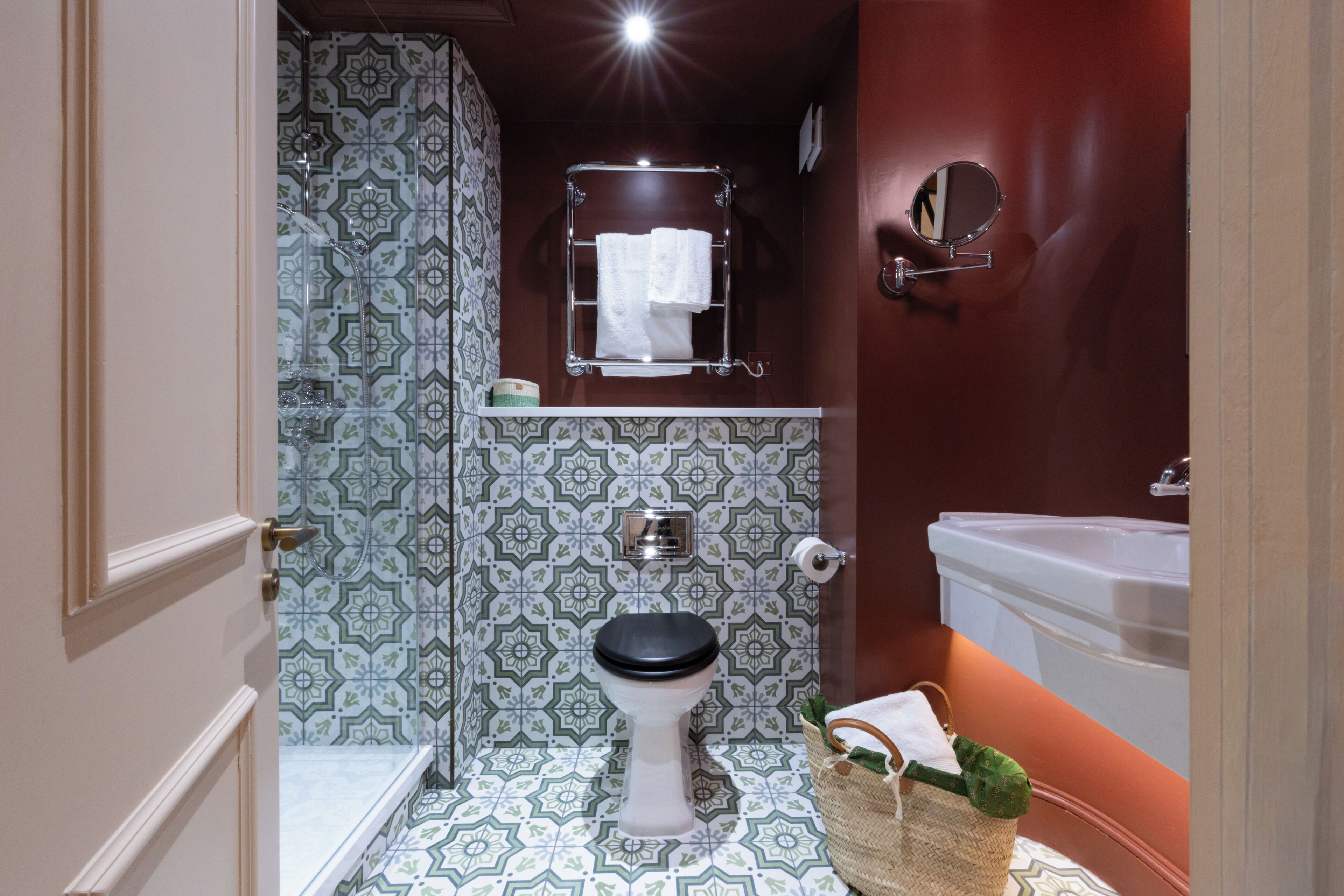 A bathroom with a patterned tile floor, a toilet, a shower, a sink, and a towel rack.