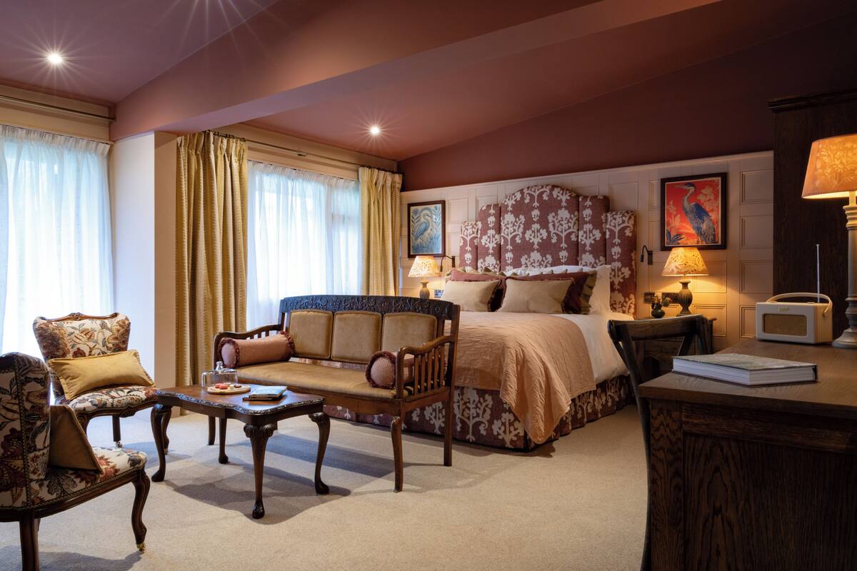 Een hotelkamer met een bed, een bank, een stoel, een tafel en een bureau met een lamp.