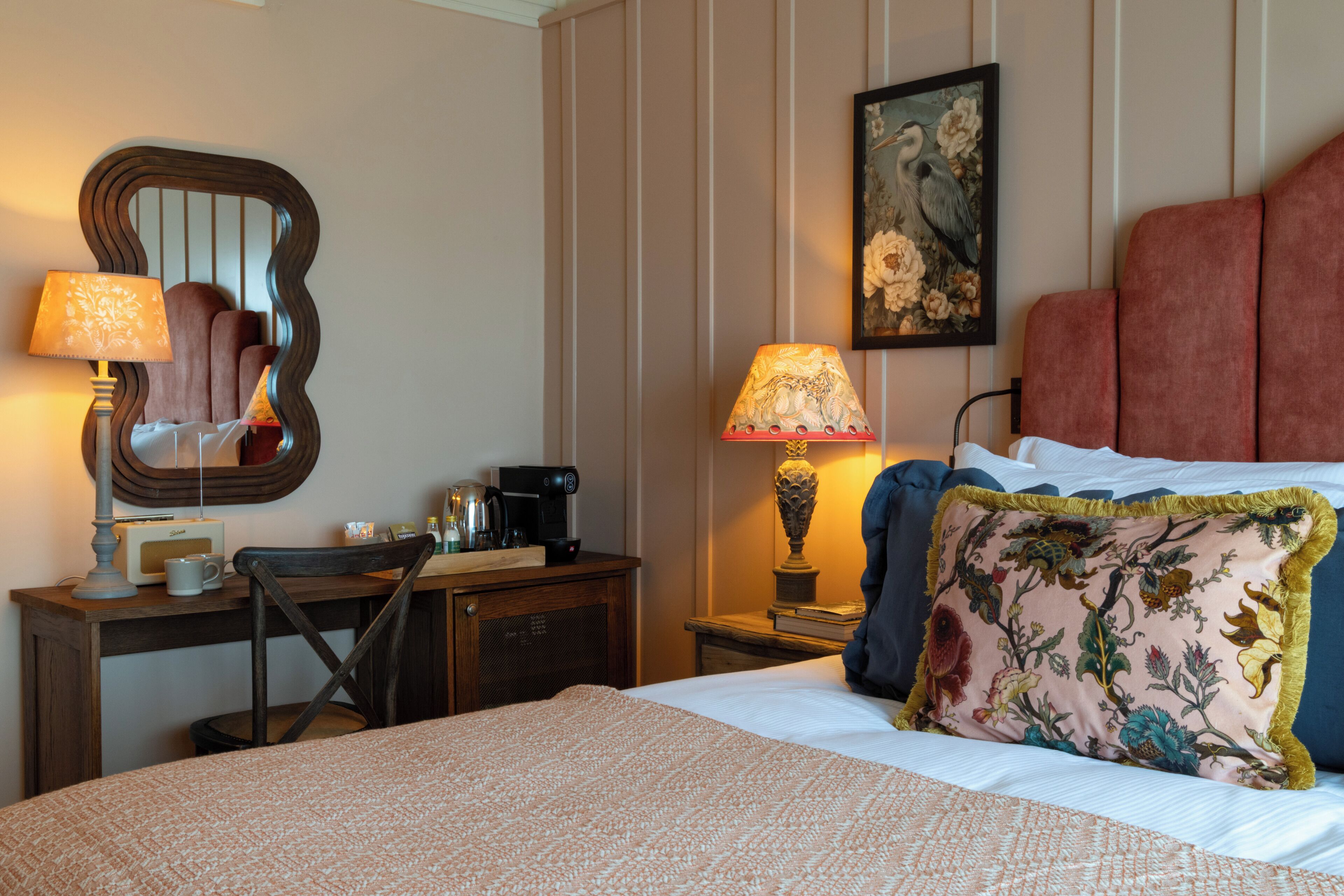 Une chambre d’hôtel avec un lit, un bureau avec une lampe, une chaise, une table de chevet avec une lampe et un tableau au mur.