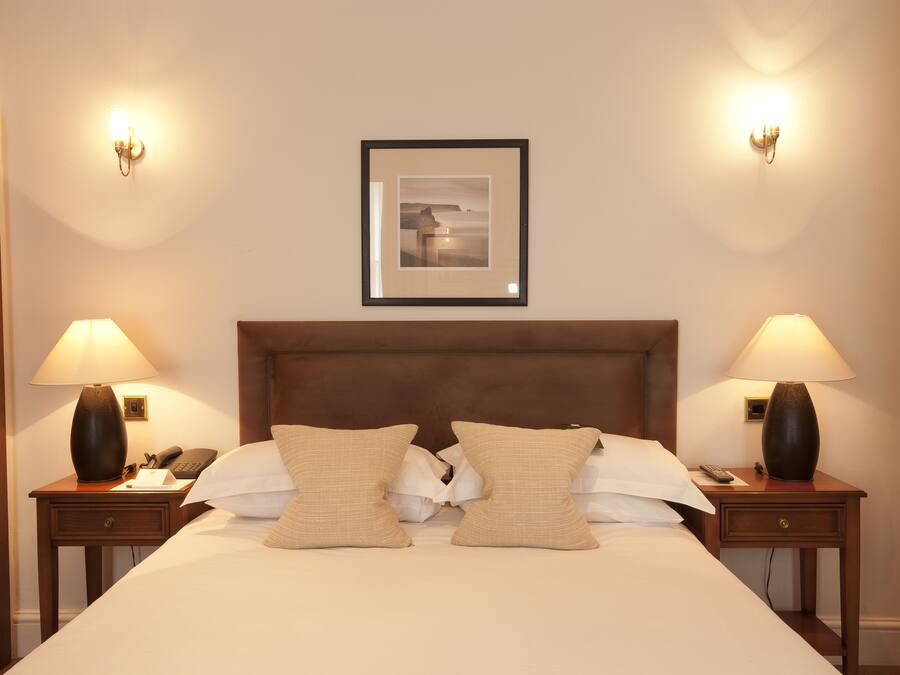 Ein Hotelzimmer mit einem großen Bett, zwei Nachttischen, einem gerahmten Bild an der Wand und zwei Wandlampen.