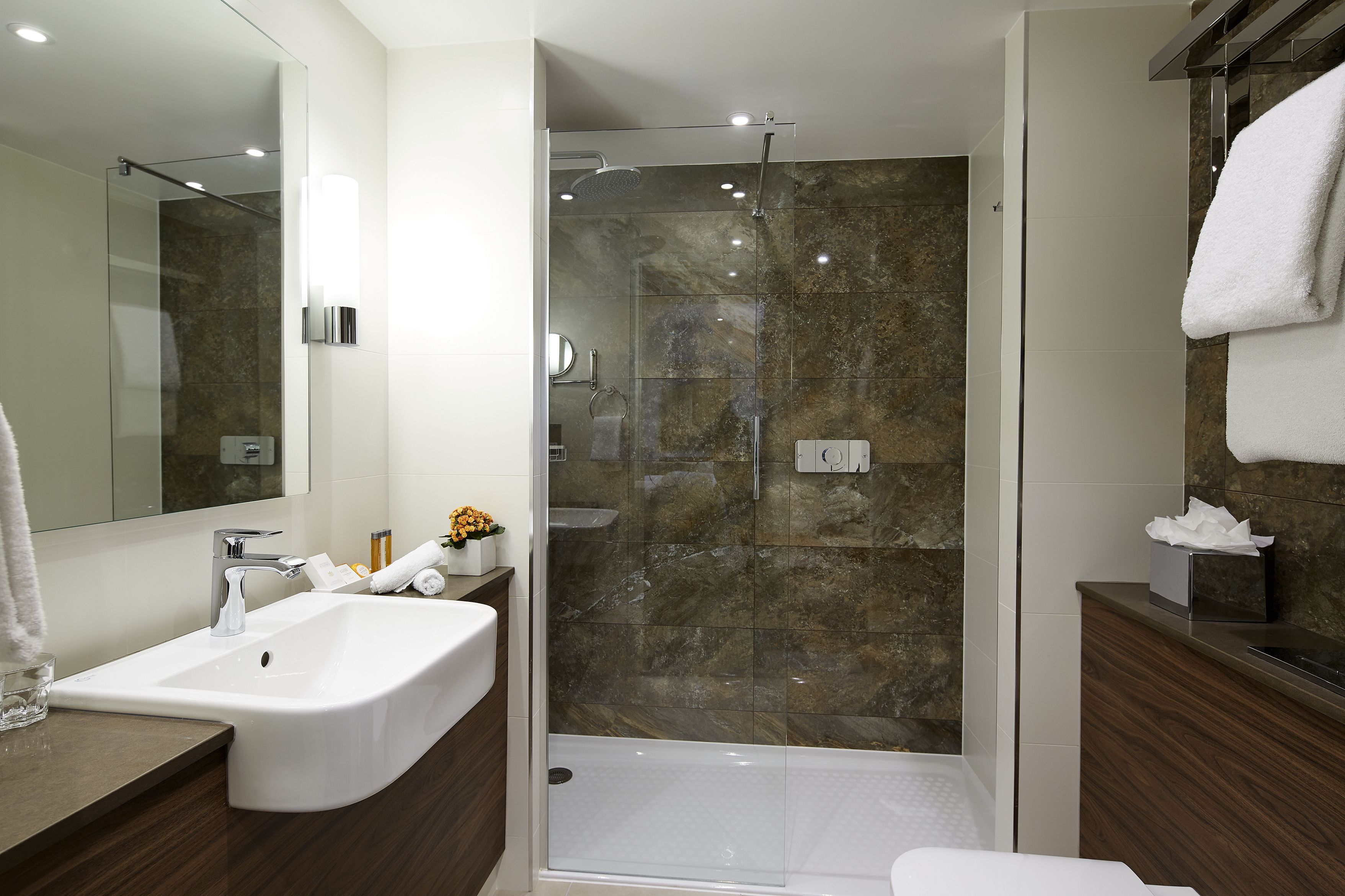 Ein modernes Badezimmer mit einer begehbaren Glasdusche, einem weißen Waschbecken und einem Holz-Waschtisch.