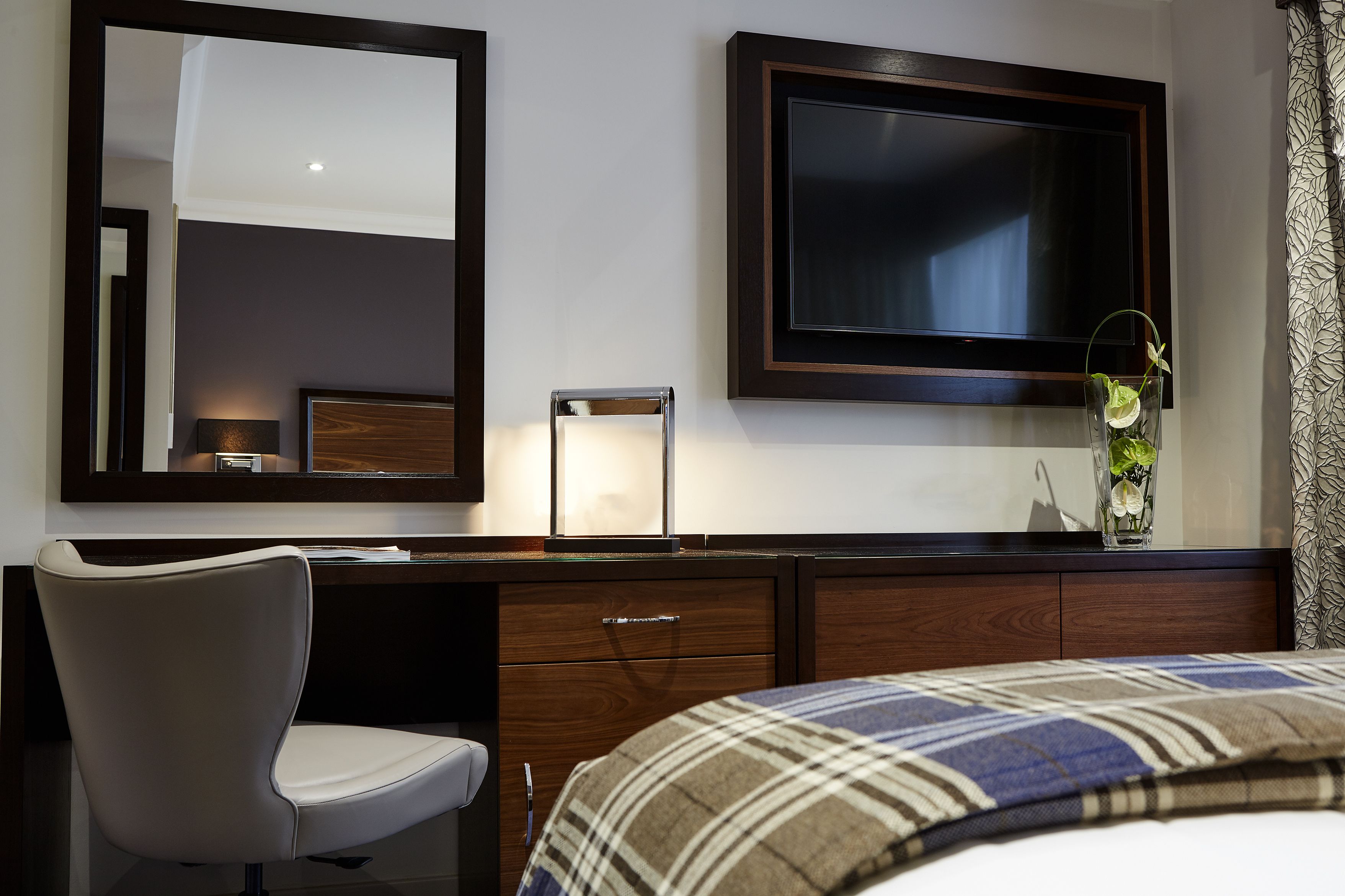 Hotellihuone, jossa on sänky, työpöytä tuolilla, televisio ja peili.