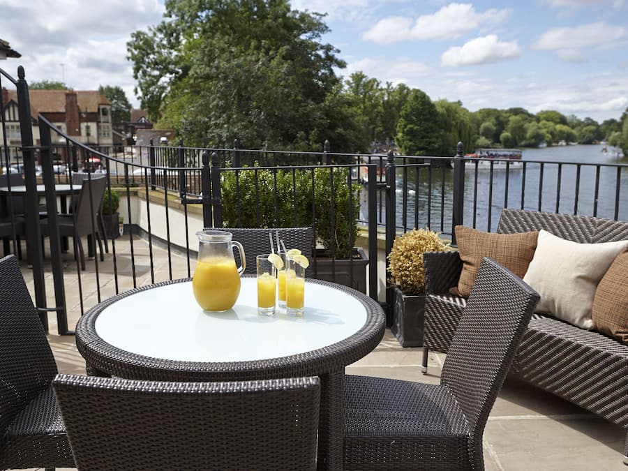 A patio with wicker furniture, a table with a pitcher of juice, and a view of a river and trees.