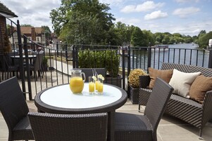 A patio with wicker furniture, a table with a pitcher of juice, and a view of a river and trees.