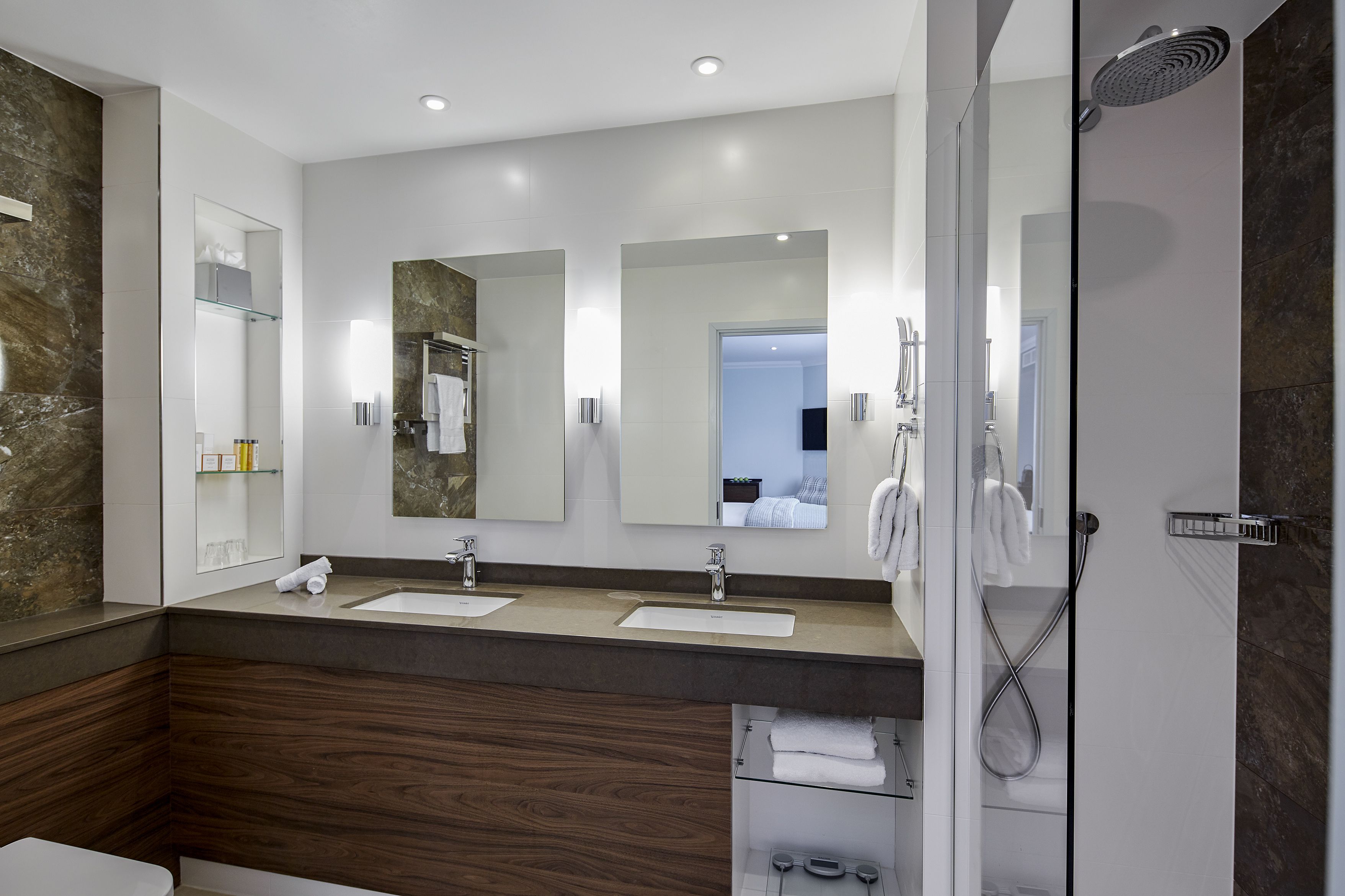 Une salle de bain moderne avec deux lavabos, une douche et des toilettes séparées par une paroi en verre.
