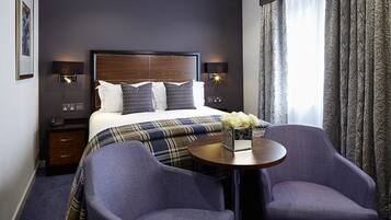 A hotel room with a large bed, two bedside tables, a small table with chairs, and a window with curtains.