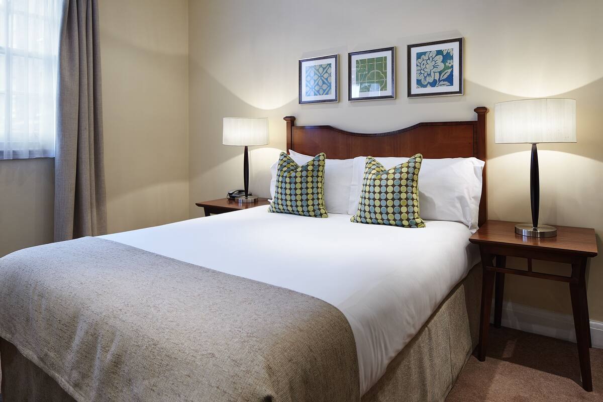 A neatly made bed with a white comforter and patterned pillows, two bedside lamps, and framed artwork on the wall.