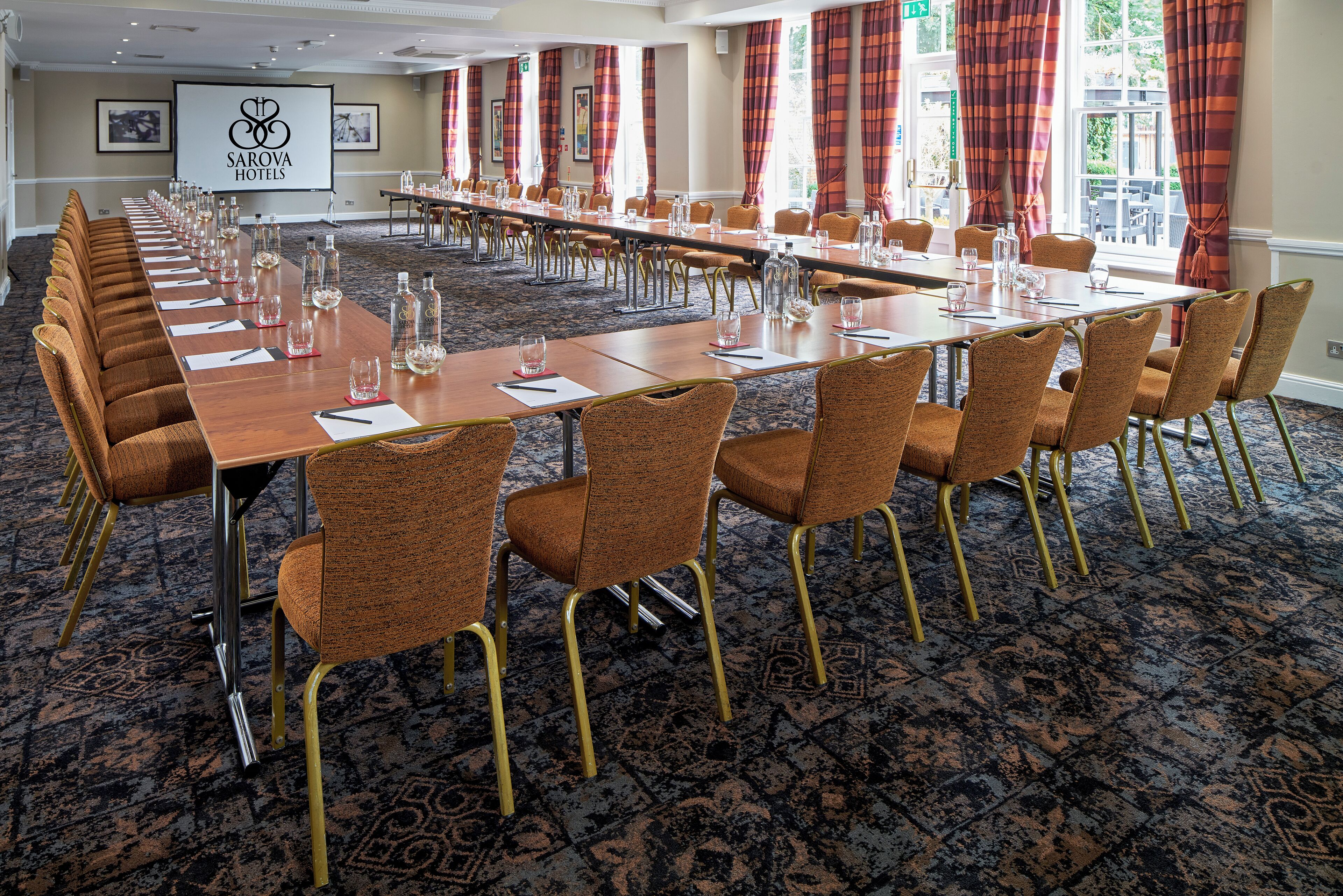 A conference room with a long table, chairs, and a projector screen displaying the hotel name.