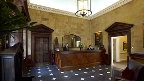 A reception area with a wooden reception desk, a large mirror, and a chandelier. - Sir Christopher Wren Hotel (Windsor)