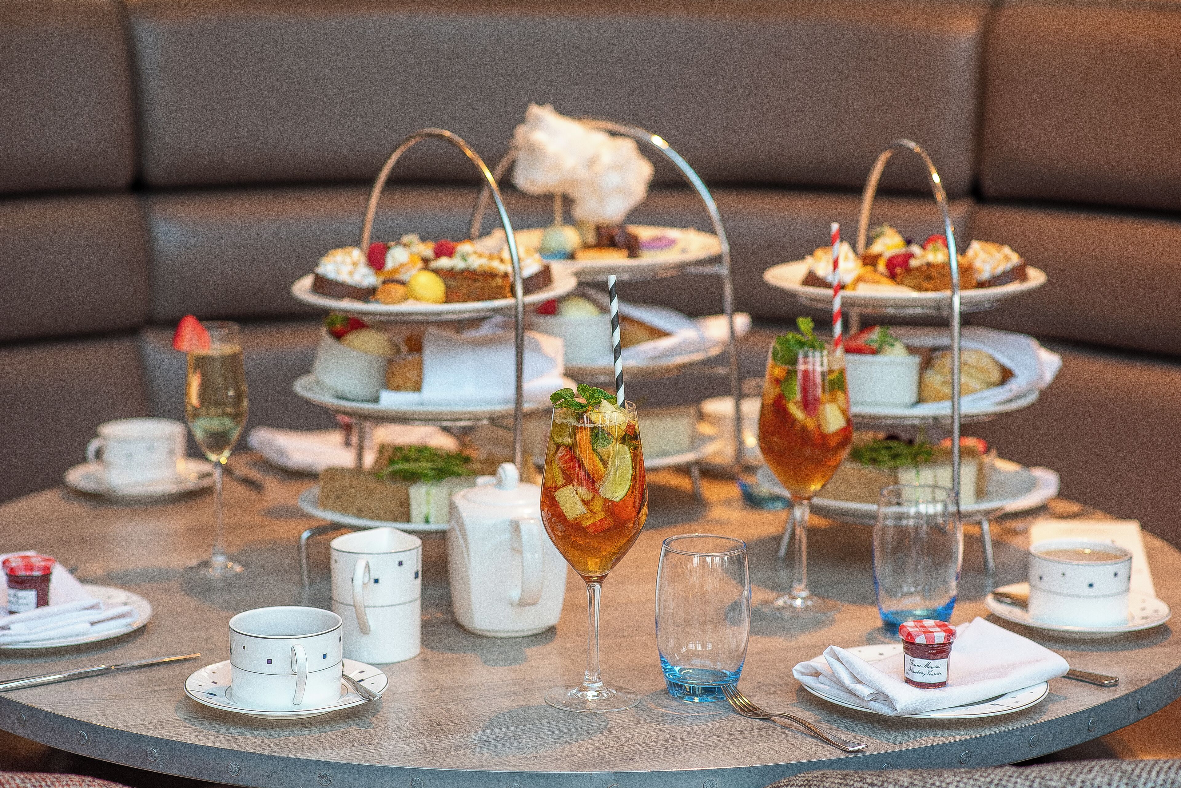 A round table with a tiered dessert stand, tea service, and a glass of iced tea.
