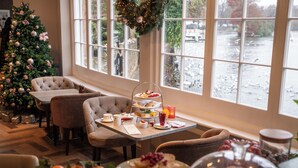 A cozy dining area with a Christmas tree, a buffet table with various food items, and a view of a river through large windows. - Sir Christopher Wren Hotel (Windsor)
