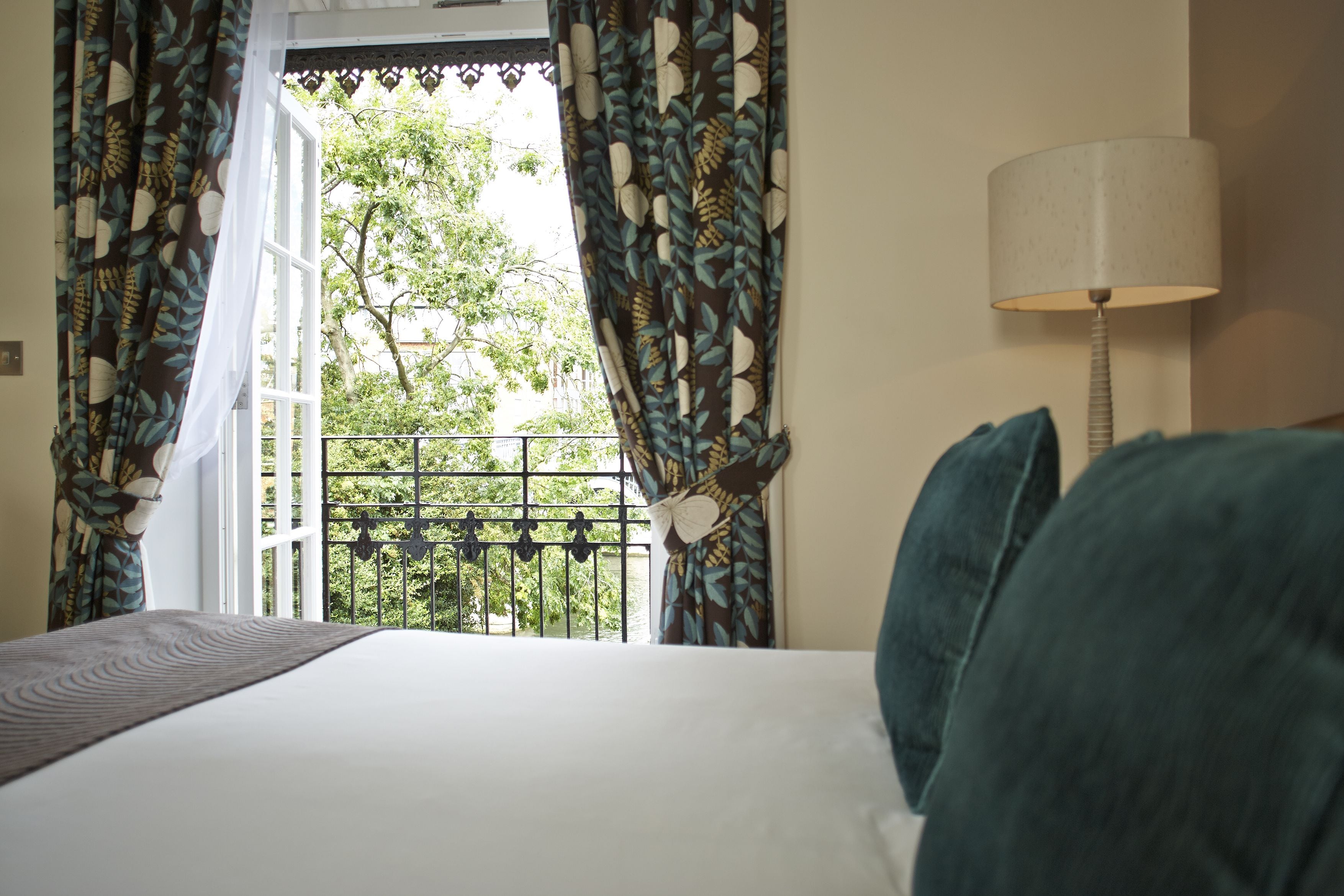 Habitación de hotel con cama, cortinas, lámpara y vistas al balcón.