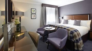 Una habitación de hotel con una cama, un escritorio con una silla, una mesita y un televisor.