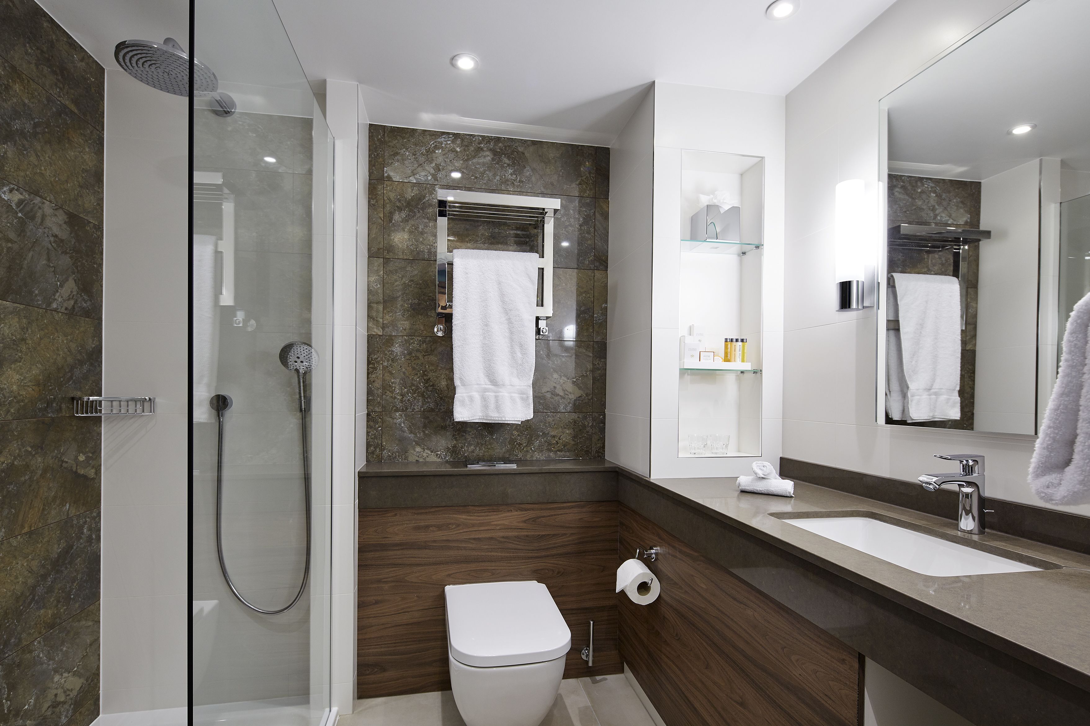 A modern bathroom with a glass-enclosed shower, a white toilet, a large mirror, and a dark wood vanity.