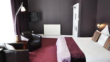 A hotel room with a bed, a chair, a desk, a lamp, and a television on the wall.