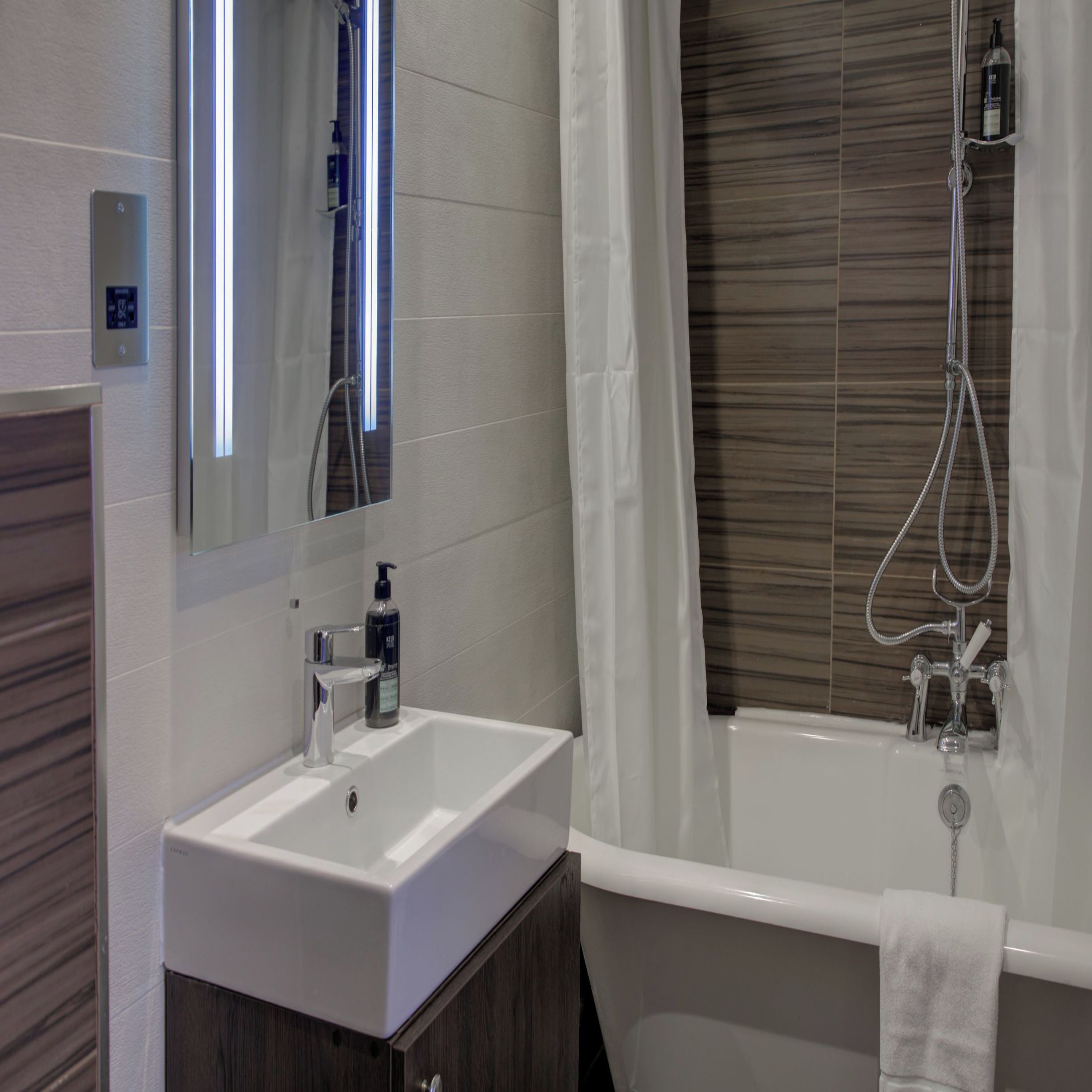 Ein modernes Badezimmer mit einem weißen Waschbecken, einem Spiegel, einer Duschkabine mit Vorhang und einem Handtuch an der Wand.