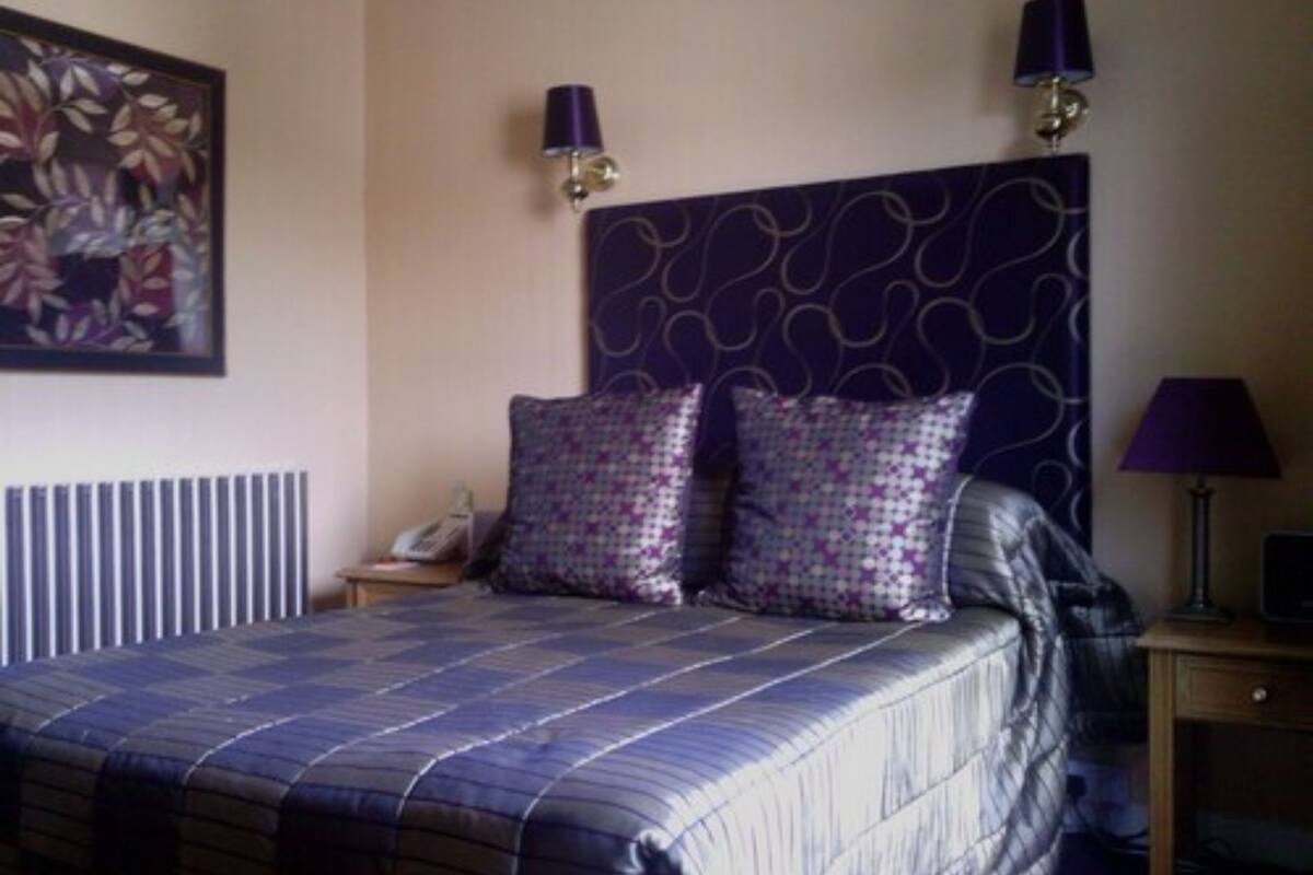 A neatly arranged bedroom with a bed, two pillows, a bedside table with a lamp, and a wall-mounted lamp.