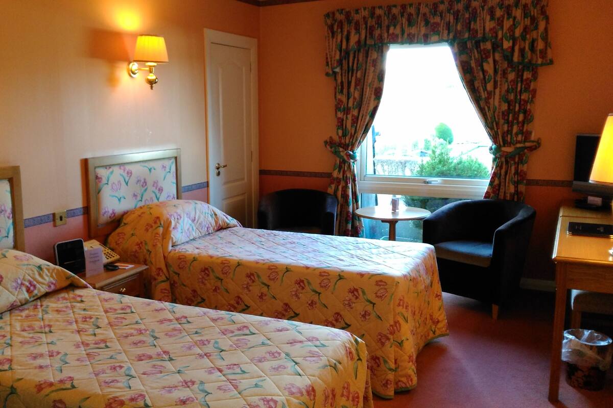 A hotel room with two beds, a desk, a chair, a small table, and a window with curtains.