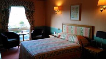 Una habitación de hotel con cama, dos sillas, una mesita y una mesita de noche.