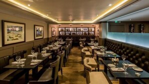 A restaurant with multiple tables and booths, framed pictures on the walls, and a bar area with shelves.