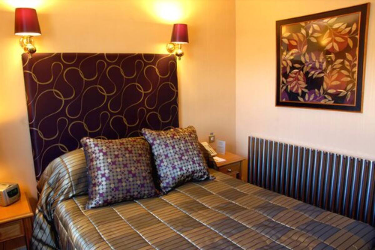 A neatly made bed with patterned bedding, two wall-mounted lamps, and a floral artwork on the wall.
