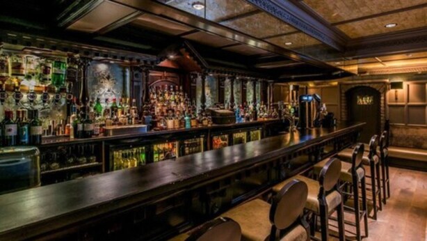 A bar with a long counter, multiple stools, and a variety of bottles and glasses.