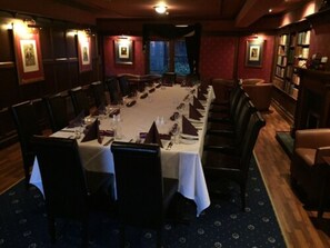Una larga mesa de comedor con sillas, rodeada de estanterías y una chimenea.