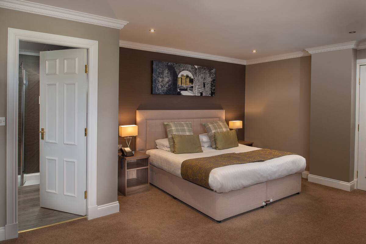 A bedroom with a bed, bedside tables, lamps, a painting, and a door.