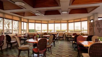 Un restaurante con varias mesas y sillas, ventanas amplias con vistas, y un suelo con diseño.