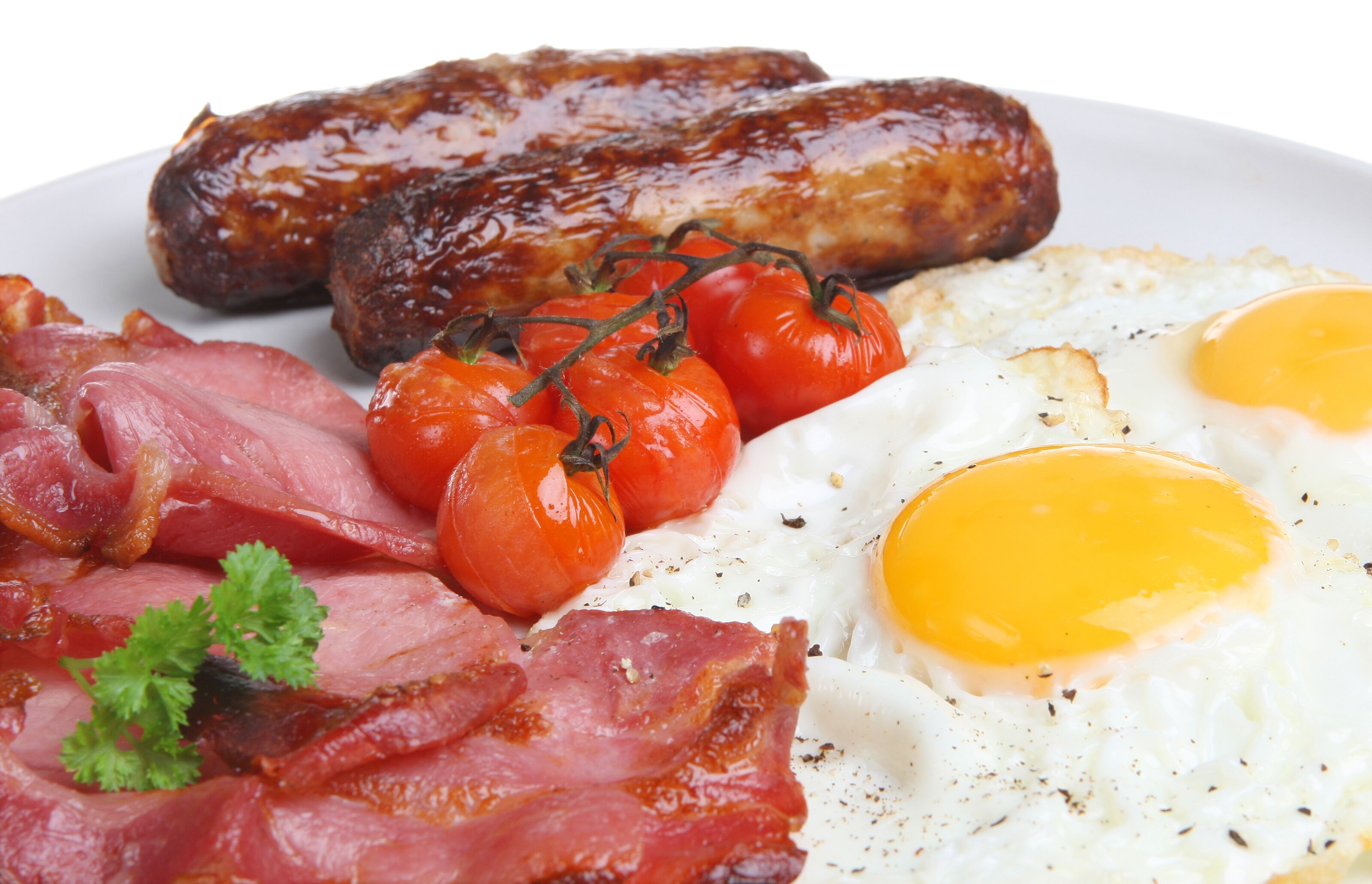 A plate of breakfast food including sausages, eggs, tomatoes, and bacon.