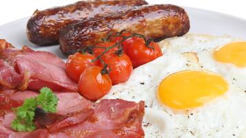 A plate of breakfast food including sausages, eggs, tomatoes, and bacon.