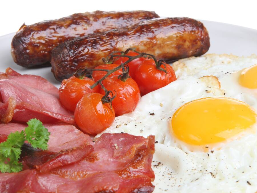 A plate of breakfast food including sausages, eggs, tomatoes, and bacon.